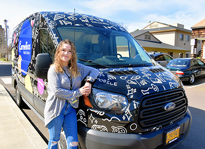 A young woman driver leans on her colorfully decorated Cornelius Library Bookmobile